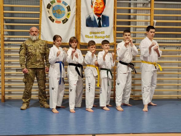 Zawodnicy TKD Dźwirzyno w doboku podczas egzaminu na stopnie, w tle flaga ITF i portret gen. Choi Hong Hi